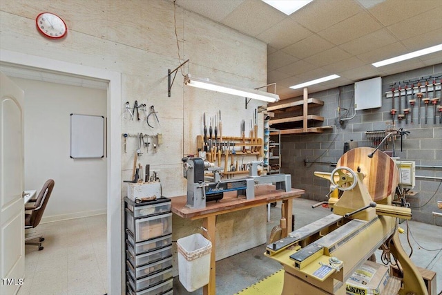 miscellaneous room with a drop ceiling, a workshop area, and concrete block wall