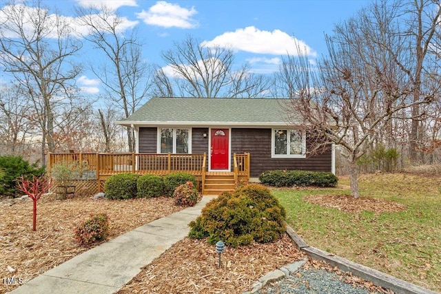 ranch-style home with a deck, a front yard, and roof with shingles