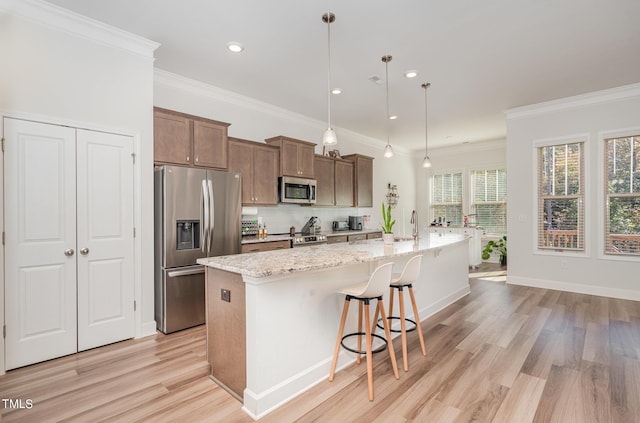 kitchen with backsplash, crown molding, light wood-style flooring, a large island with sink, and appliances with stainless steel finishes