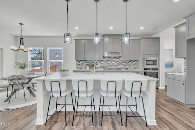 kitchen featuring a sink, stainless steel appliances, gray cabinetry, under cabinet range hood, and backsplash