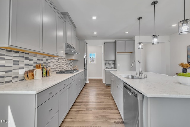 kitchen featuring light wood finished floors, under cabinet range hood, gray cabinets, stainless steel appliances, and a sink