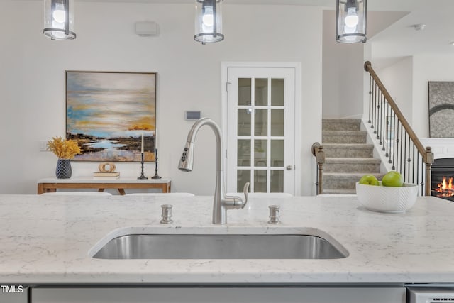 kitchen with a glass covered fireplace, hanging light fixtures, light stone countertops, and a sink