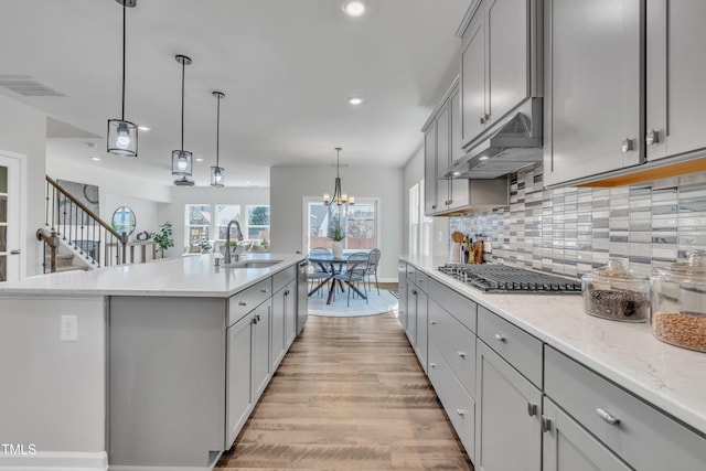 kitchen with a sink, gray cabinetry, under cabinet range hood, and stainless steel gas cooktop