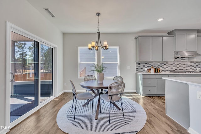 dining room featuring a notable chandelier, baseboards, visible vents, and light wood finished floors