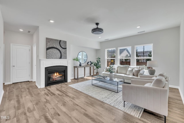 living room featuring a glass covered fireplace, recessed lighting, baseboards, and wood finished floors