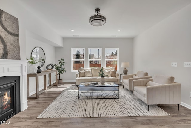 living room with baseboards, wood finished floors, visible vents, and a glass covered fireplace