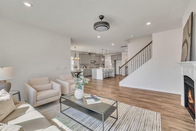 living area with a chandelier, stairs, a lit fireplace, recessed lighting, and light wood-style flooring