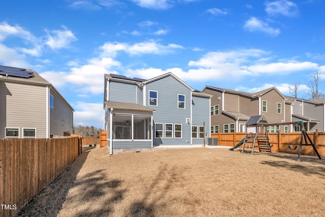 back of house featuring roof mounted solar panels, a fenced backyard, a playground, a residential view, and a sunroom