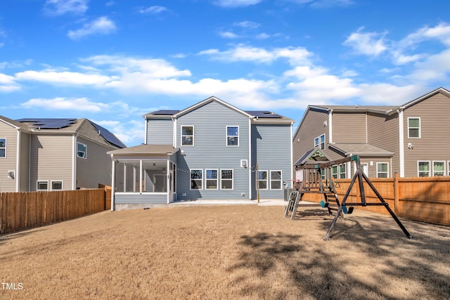 rear view of house with a playground, a sunroom, roof mounted solar panels, a yard, and a fenced backyard