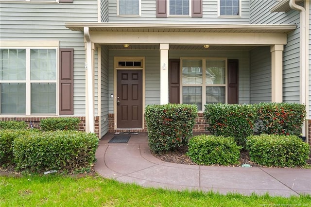 view of exterior entry featuring brick siding and a porch