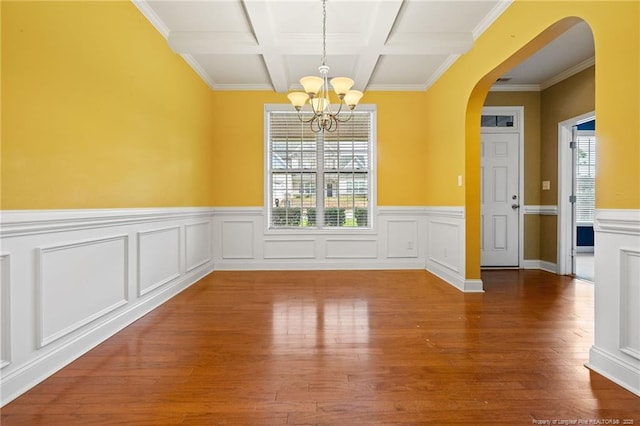 empty room featuring a wealth of natural light, a notable chandelier, arched walkways, and wood finished floors