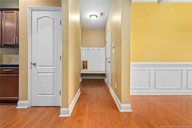 corridor featuring visible vents, baseboards, a wainscoted wall, light wood-type flooring, and a decorative wall