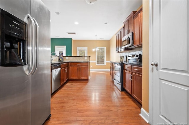 kitchen featuring tasteful backsplash, light wood finished floors, brown cabinets, stainless steel appliances, and a sink