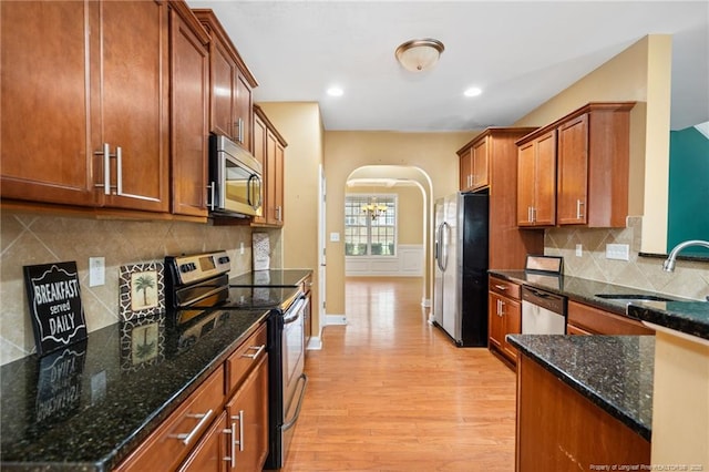 kitchen with light wood finished floors, brown cabinets, appliances with stainless steel finishes, arched walkways, and a sink