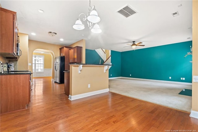 kitchen featuring dark countertops, visible vents, brown cabinetry, freestanding refrigerator, and arched walkways