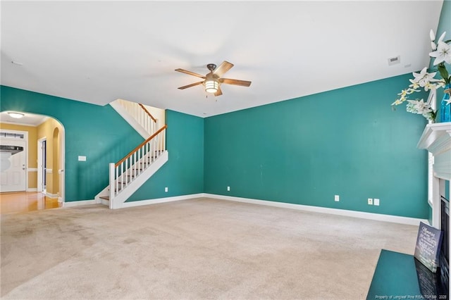 unfurnished living room with arched walkways, a fireplace with flush hearth, stairway, and carpet floors