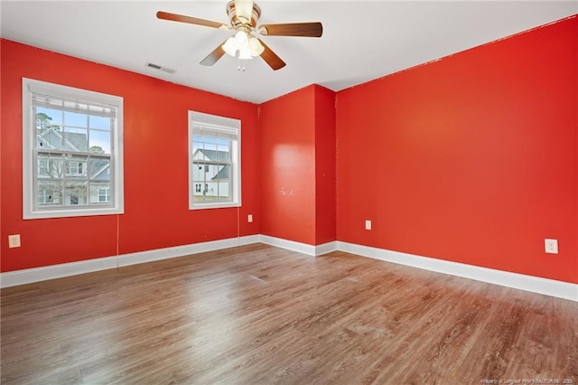 spare room with a ceiling fan, wood finished floors, visible vents, and baseboards