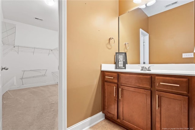 bathroom with visible vents, baseboards, a walk in closet, and vanity