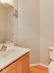 bathroom featuring baseboards, toilet, wood finished floors, and vanity