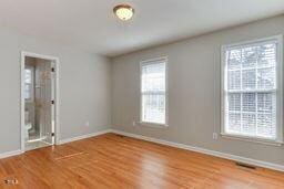 unfurnished bedroom featuring visible vents, multiple windows, wood finished floors, and baseboards