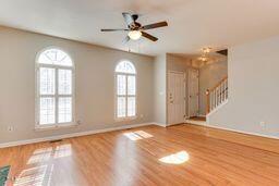 unfurnished living room featuring a ceiling fan, stairs, wood finished floors, and baseboards