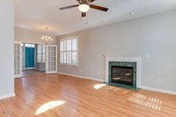 unfurnished living room featuring ceiling fan with notable chandelier, a fireplace with flush hearth, wood finished floors, and baseboards