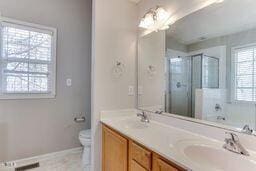 bathroom featuring toilet, a sink, a shower stall, double vanity, and baseboards