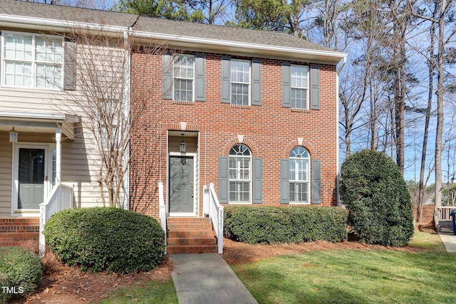 view of front of property featuring entry steps, a front yard, brick siding, and roof with shingles