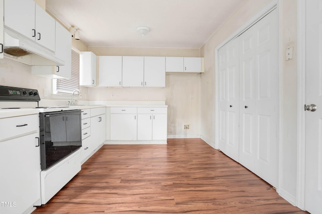 kitchen with range with electric cooktop, a sink, wood finished floors, white cabinets, and light countertops