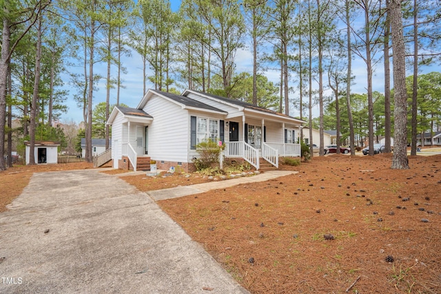 ranch-style home featuring driveway, a shed, covered porch, an outdoor structure, and crawl space