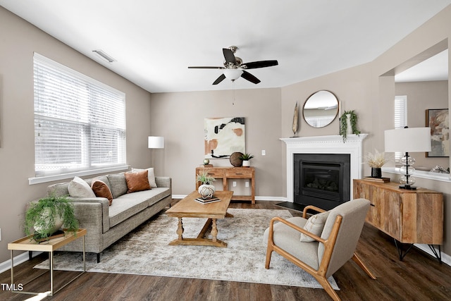 living room featuring visible vents, a fireplace with flush hearth, baseboards, and wood finished floors