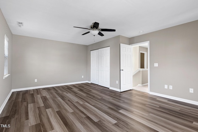 unfurnished bedroom with a closet, baseboards, dark wood finished floors, and a ceiling fan