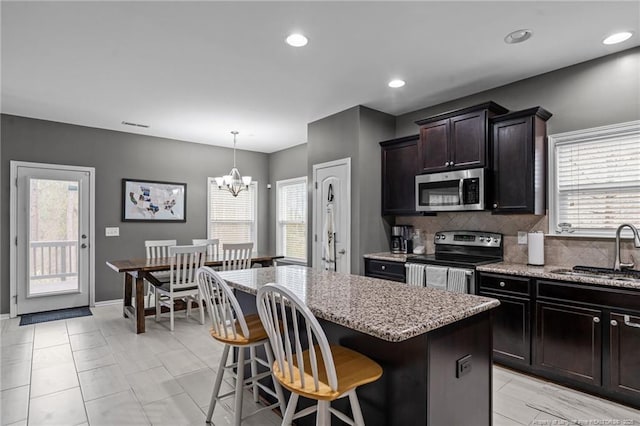 kitchen with tasteful backsplash, a center island, light stone countertops, appliances with stainless steel finishes, and a sink