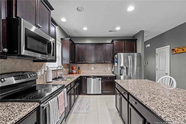 kitchen featuring a sink, stainless steel appliances, light stone counters, and dark brown cabinetry