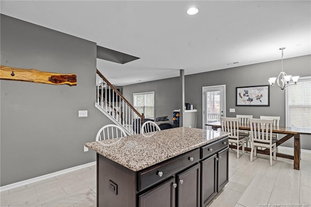 kitchen with a notable chandelier, decorative light fixtures, a kitchen island, baseboards, and light stone countertops