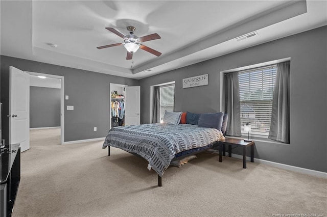 bedroom with a spacious closet, visible vents, baseboards, light colored carpet, and a raised ceiling