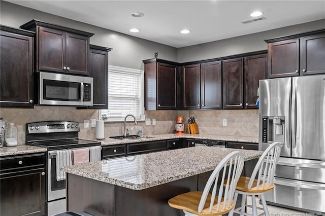 kitchen with a breakfast bar area, visible vents, a sink, dark brown cabinets, and appliances with stainless steel finishes