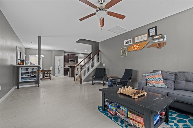 living room with stairway, baseboards, visible vents, and ceiling fan