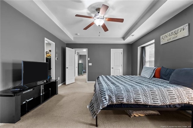 bedroom with a tray ceiling, baseboards, light colored carpet, and ceiling fan