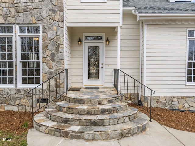 view of exterior entry featuring crawl space, stone siding, and a shingled roof