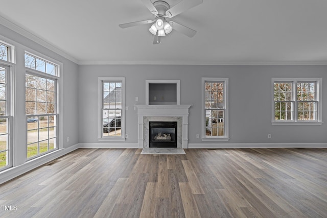 unfurnished living room with a high end fireplace, crown molding, ceiling fan, baseboards, and wood finished floors