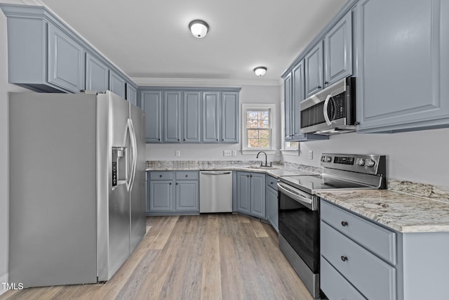 kitchen with light wood finished floors, gray cabinetry, crown molding, appliances with stainless steel finishes, and a sink