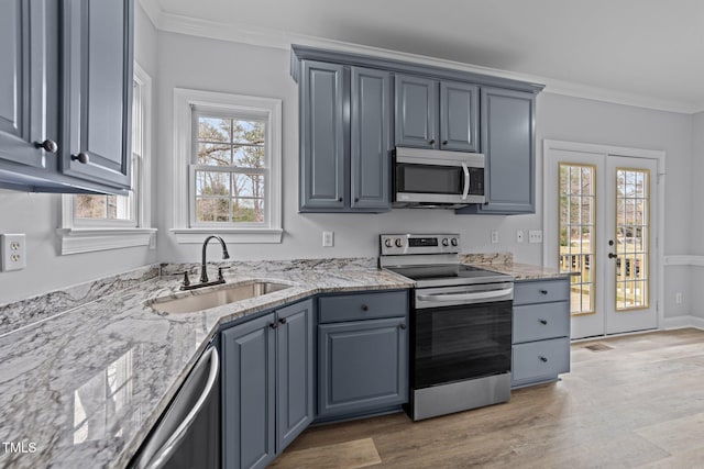 kitchen with ornamental molding, light stone countertops, appliances with stainless steel finishes, and a sink