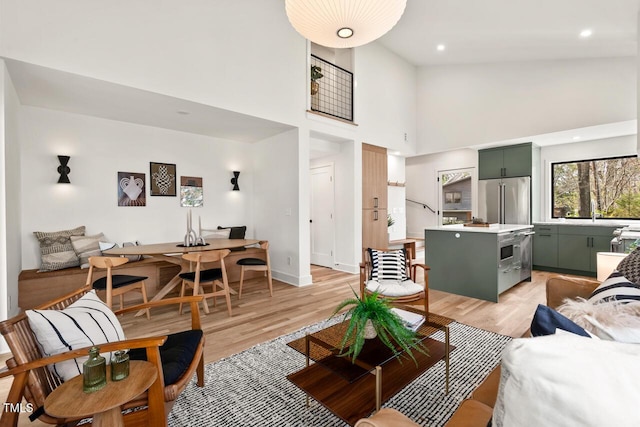 living area with light wood finished floors, recessed lighting, a high ceiling, and baseboards