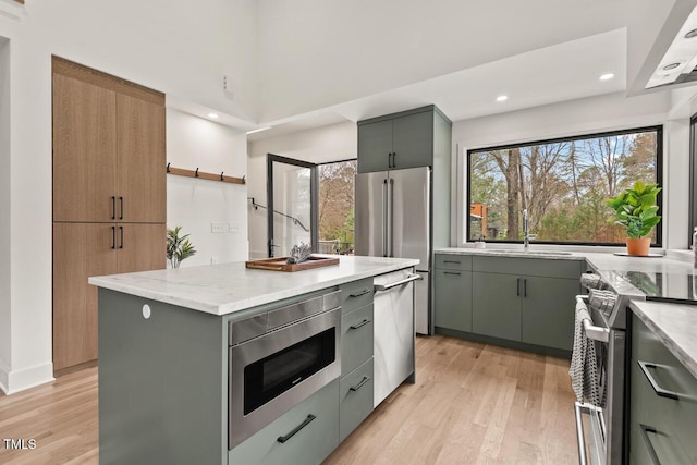 kitchen with gray cabinets, a sink, appliances with stainless steel finishes, light wood finished floors, and light stone countertops