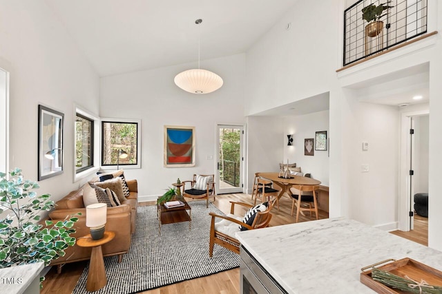 living room with baseboards, high vaulted ceiling, and light wood-style flooring