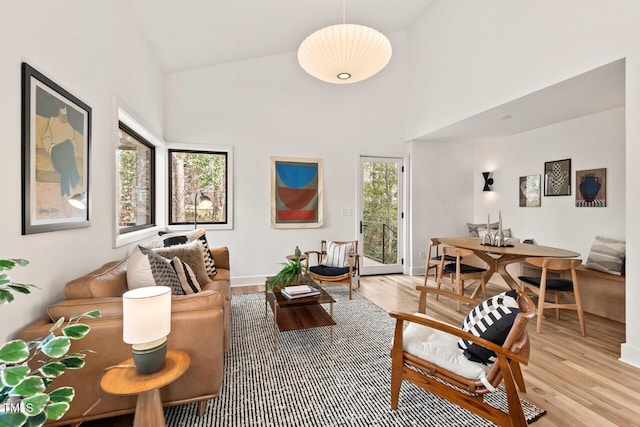 living room with baseboards, light wood-style floors, and high vaulted ceiling