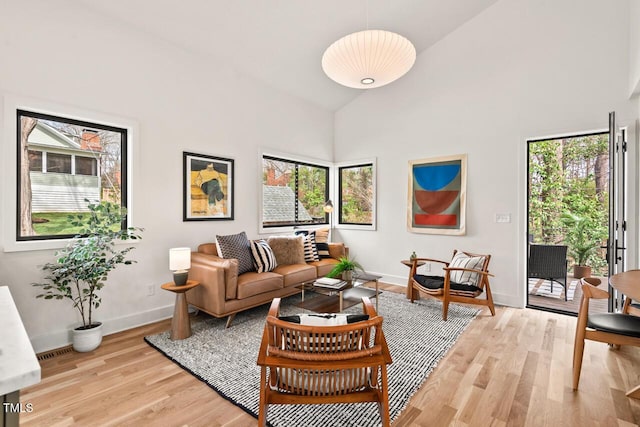 living room featuring baseboards, plenty of natural light, light wood-style floors, and high vaulted ceiling