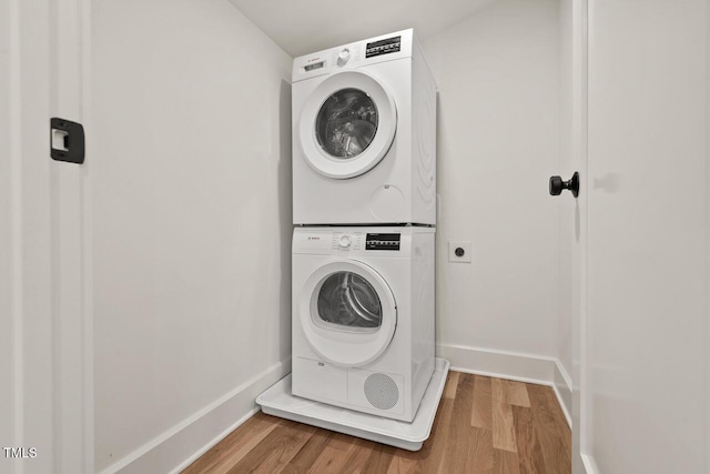 laundry area with laundry area, light wood-style flooring, baseboards, and stacked washing maching and dryer