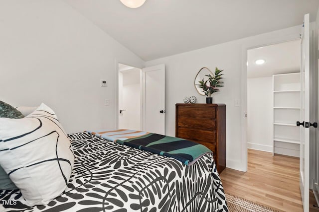 bedroom with light wood-type flooring, baseboards, and vaulted ceiling